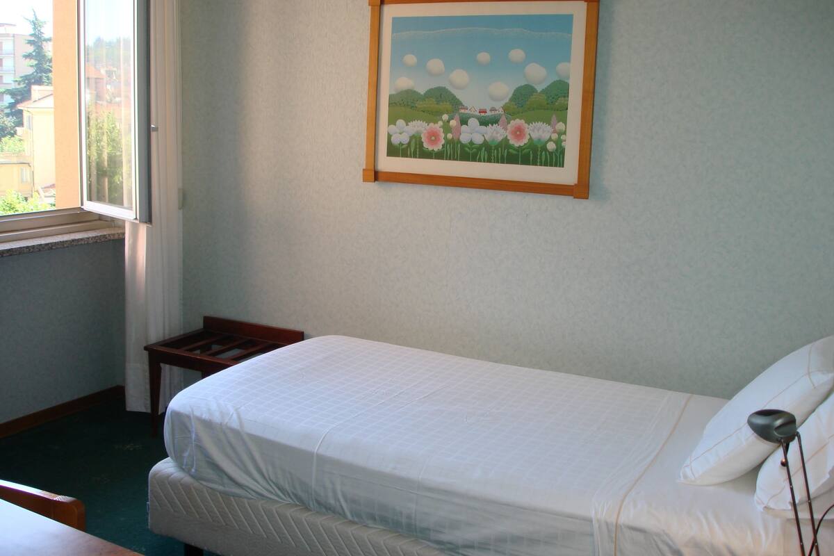 A bedroom with a bed, a nightstand, a window, and a painting on the wall.
