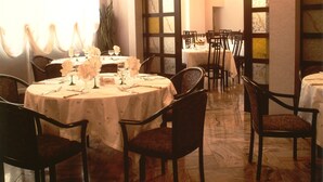 A dining area with round tables, chairs, and a large window with curtains. - Ariston (Acqui Terme)