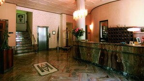 A lobby with a marble reception desk, a staircase, and a large chandelier. - Ariston (Acqui Terme)