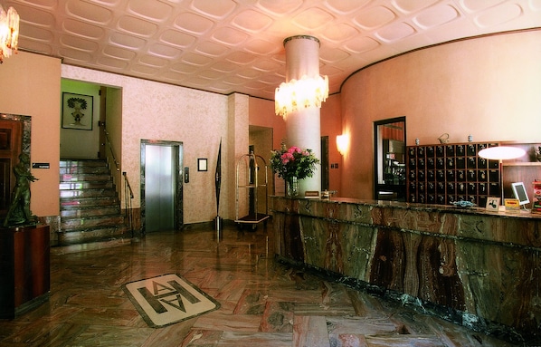 A lobby with a marble reception desk, a staircase, and a large chandelier.