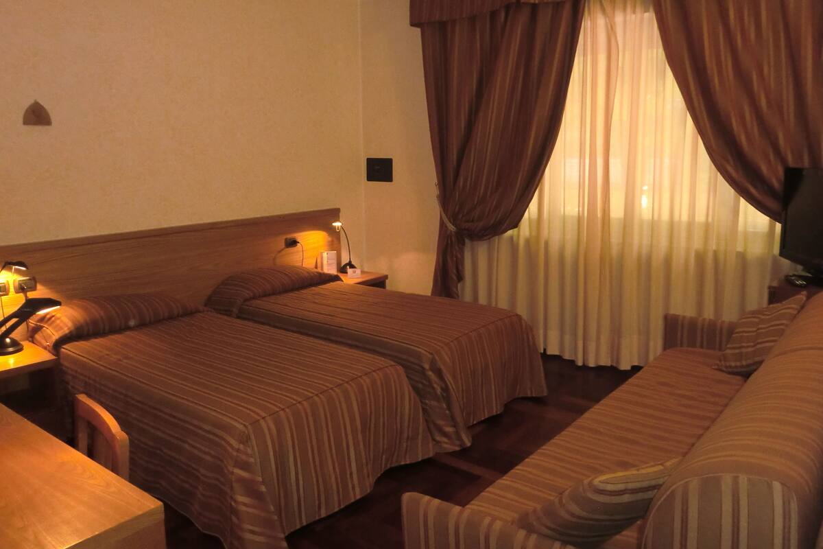 A hotel room with two beds, a sofa, a desk, and a TV.