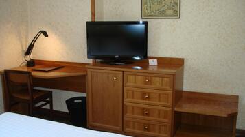 A hotel room with a wooden desk, a television, a chair, a bed, and a map on the wall.