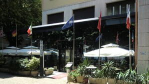 A hotel entrance with outdoor seating, flags, and potted plants. - Ariston (Acqui Terme)