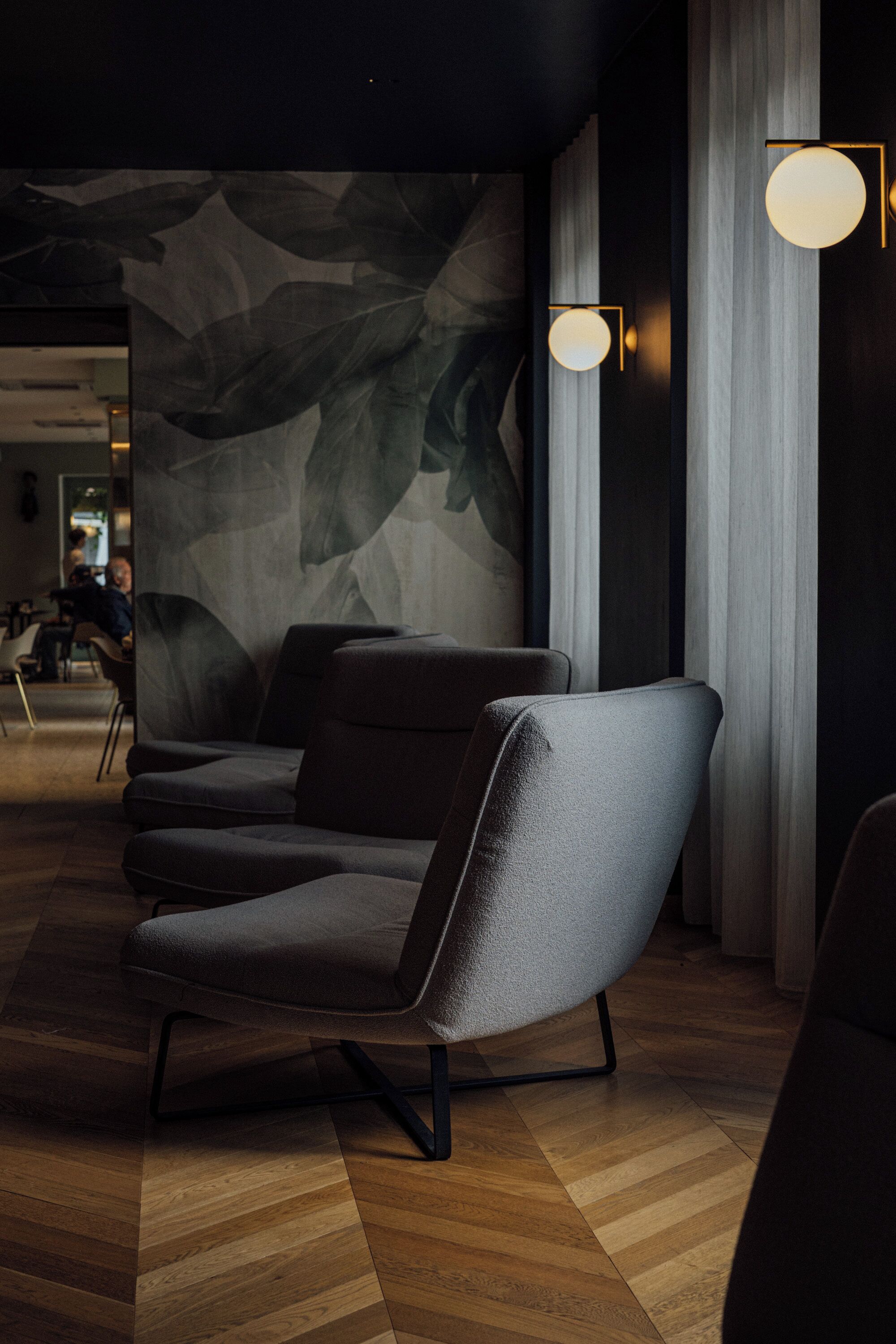 A modern interior with a dark-colored sofa, a patterned wall, and a wooden floor.