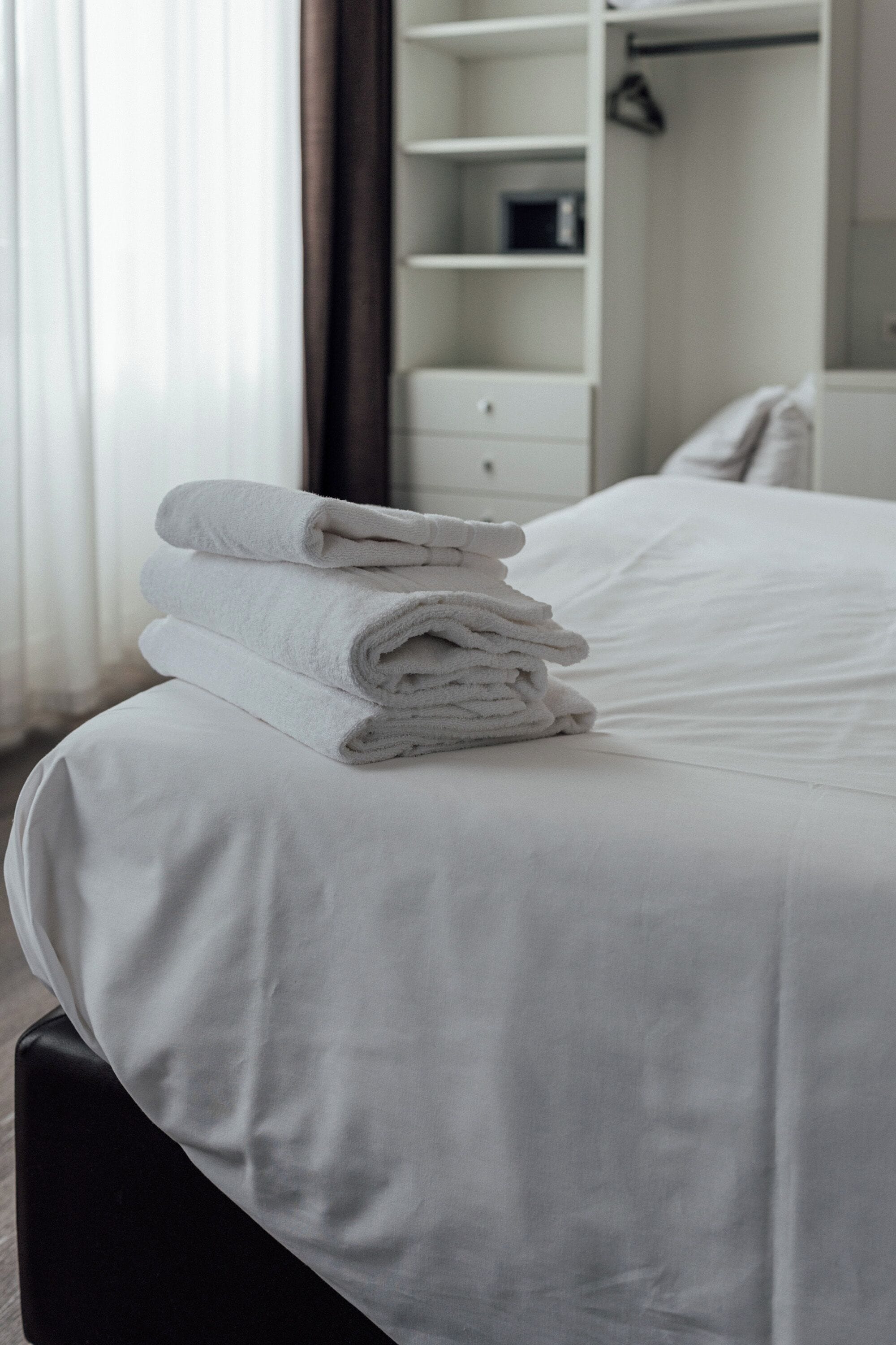 A neatly made bed with white linens and a stack of folded towels.