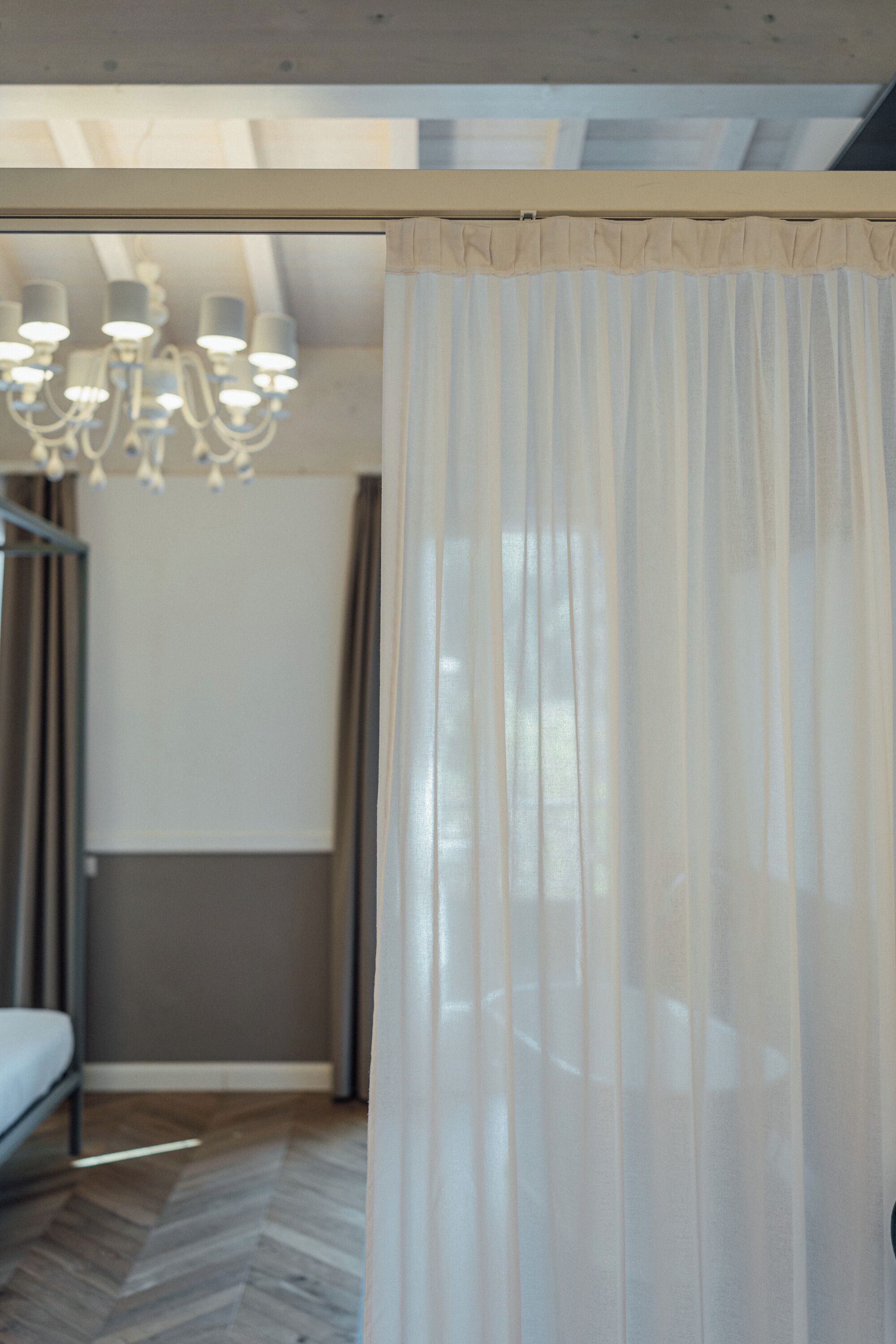 A room with a bed, a chandelier, and sheer curtains.