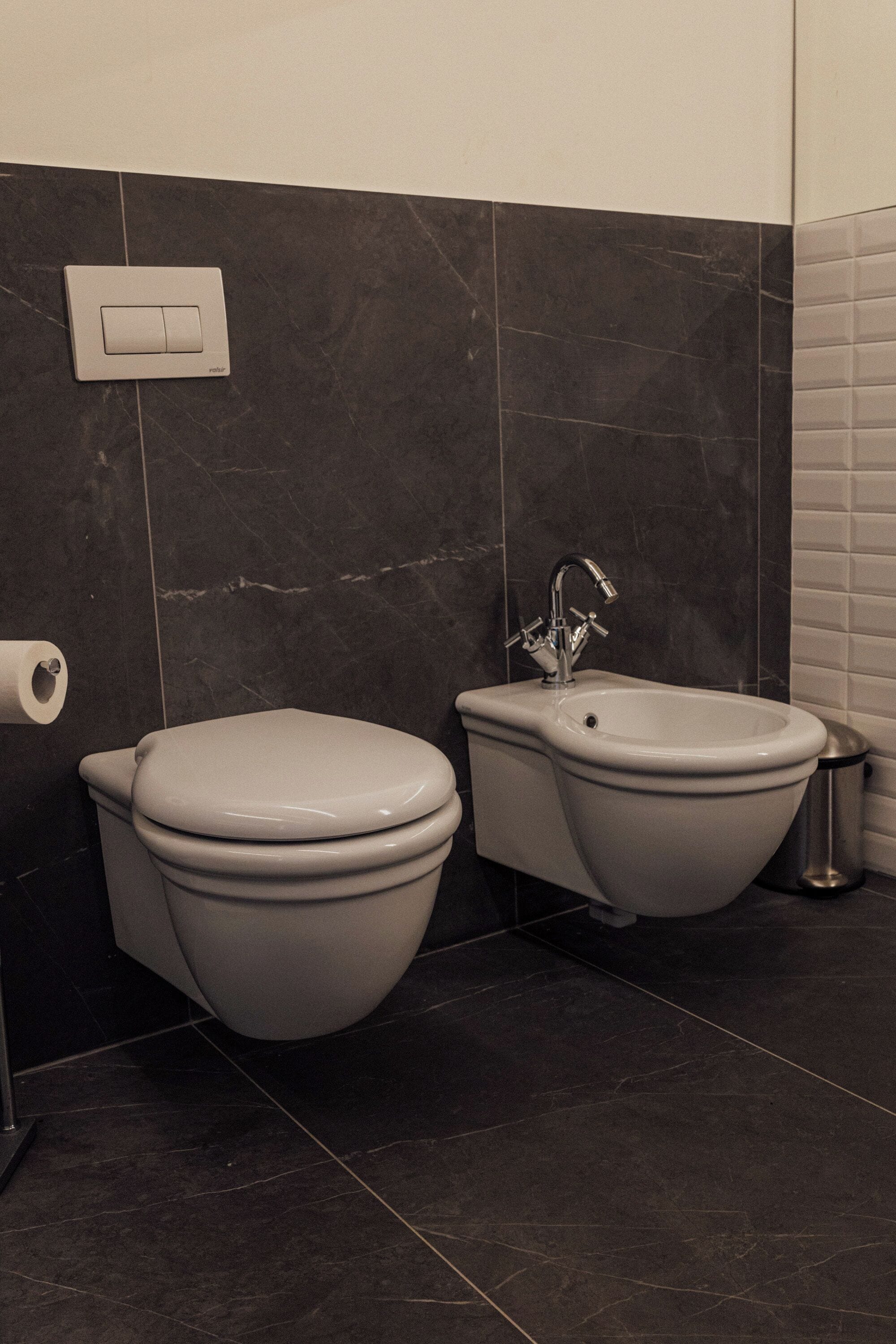Un baño con inodoro, bidé y un sistema de descarga en la pared.