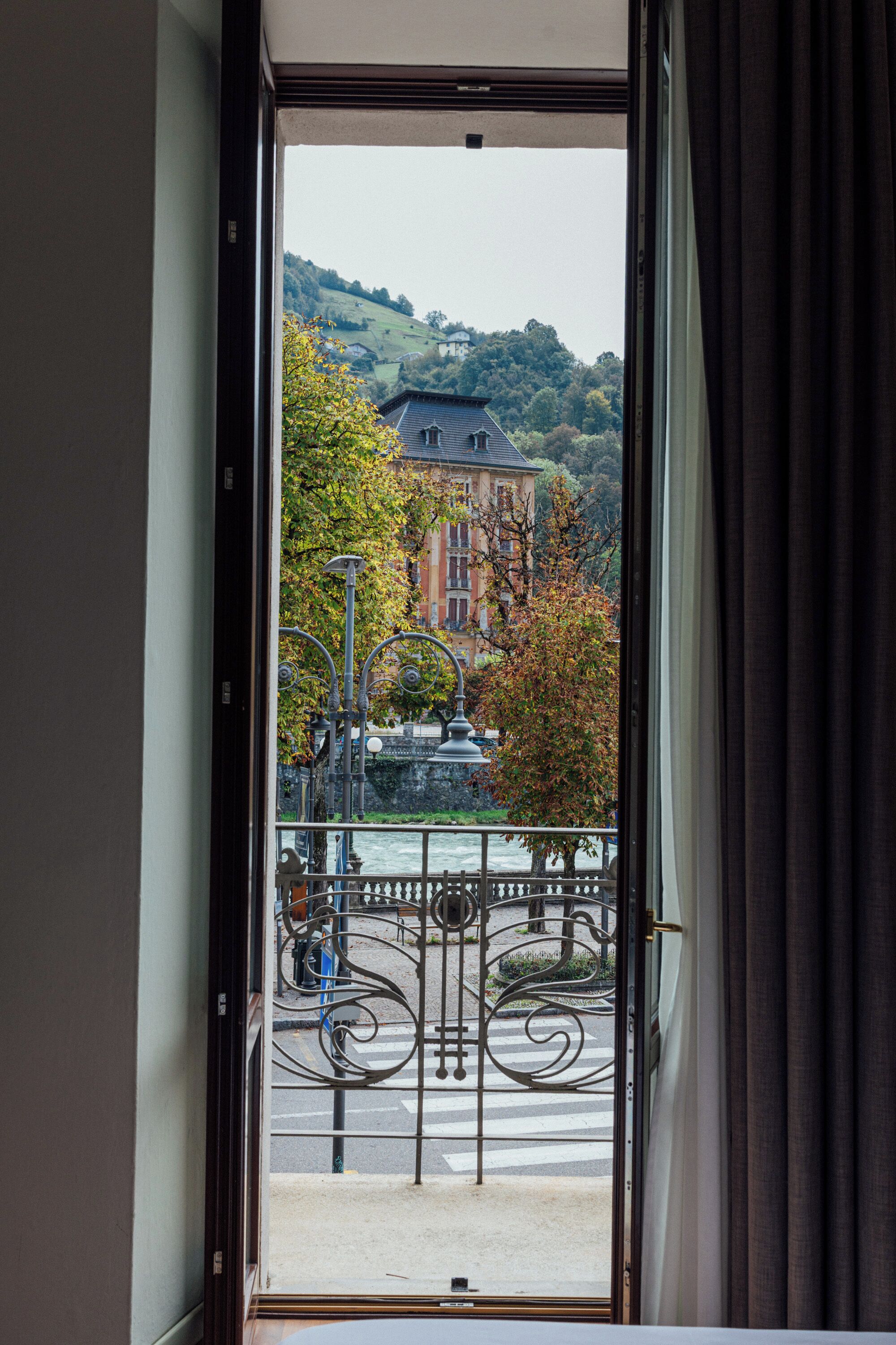 A view from a room through an open door, featuring a street with a bridge, a building with a red facade, and a hill in the background.