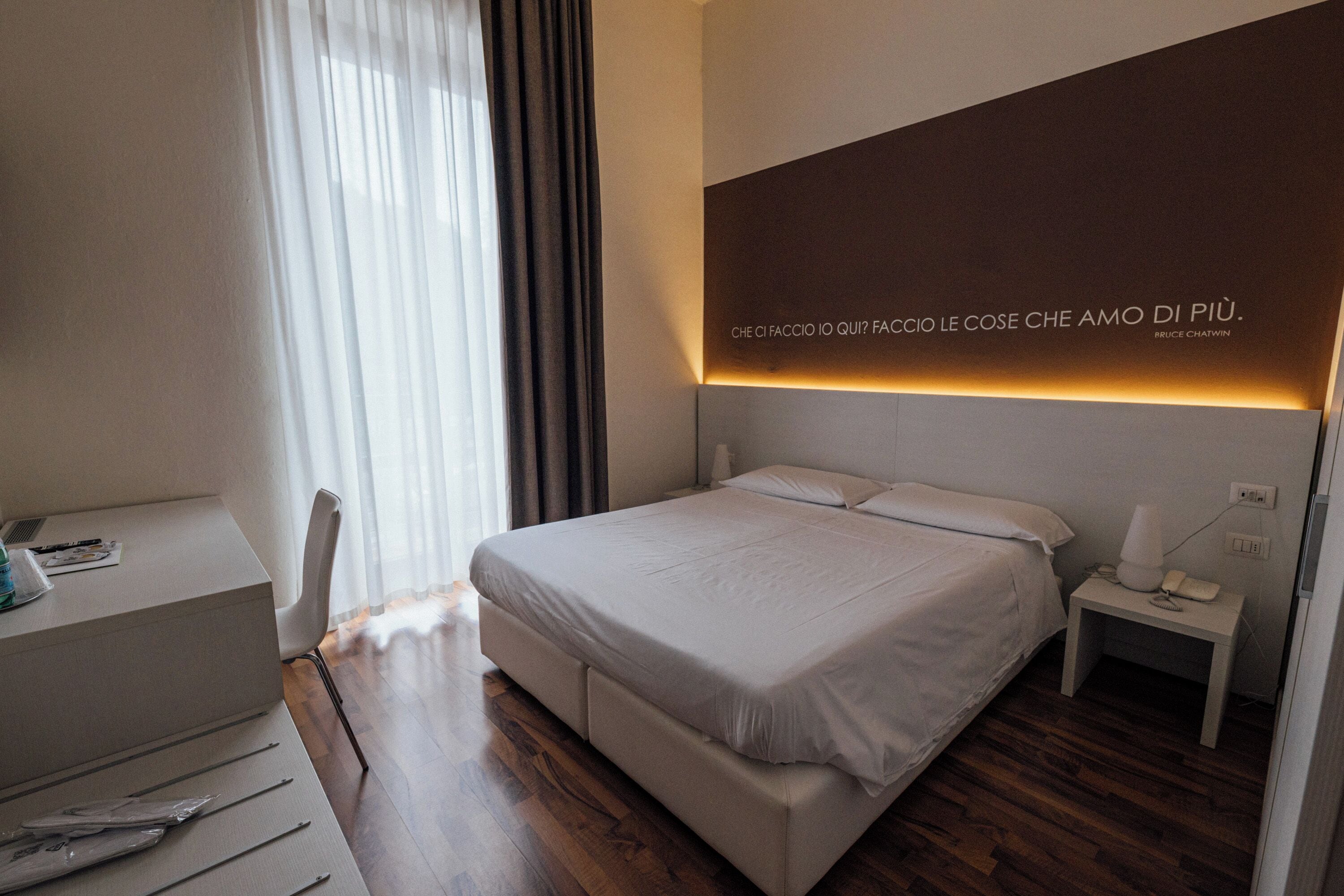 Een moderne hotelkamer met een groot bed, nachtkastje en een bureau met stoel.