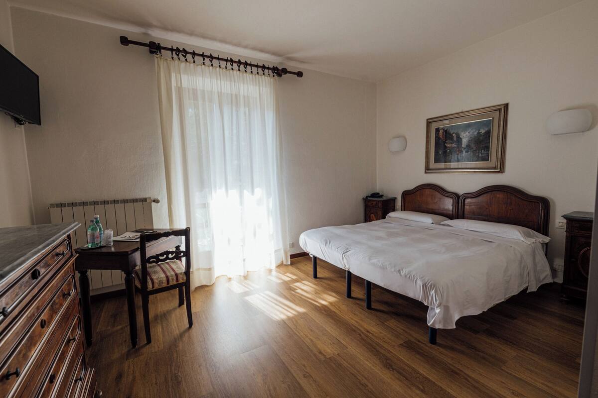 Un dormitorio con cama de madera, un escritorio con silla, televisor en la pared y un cuadro sobre la cama.