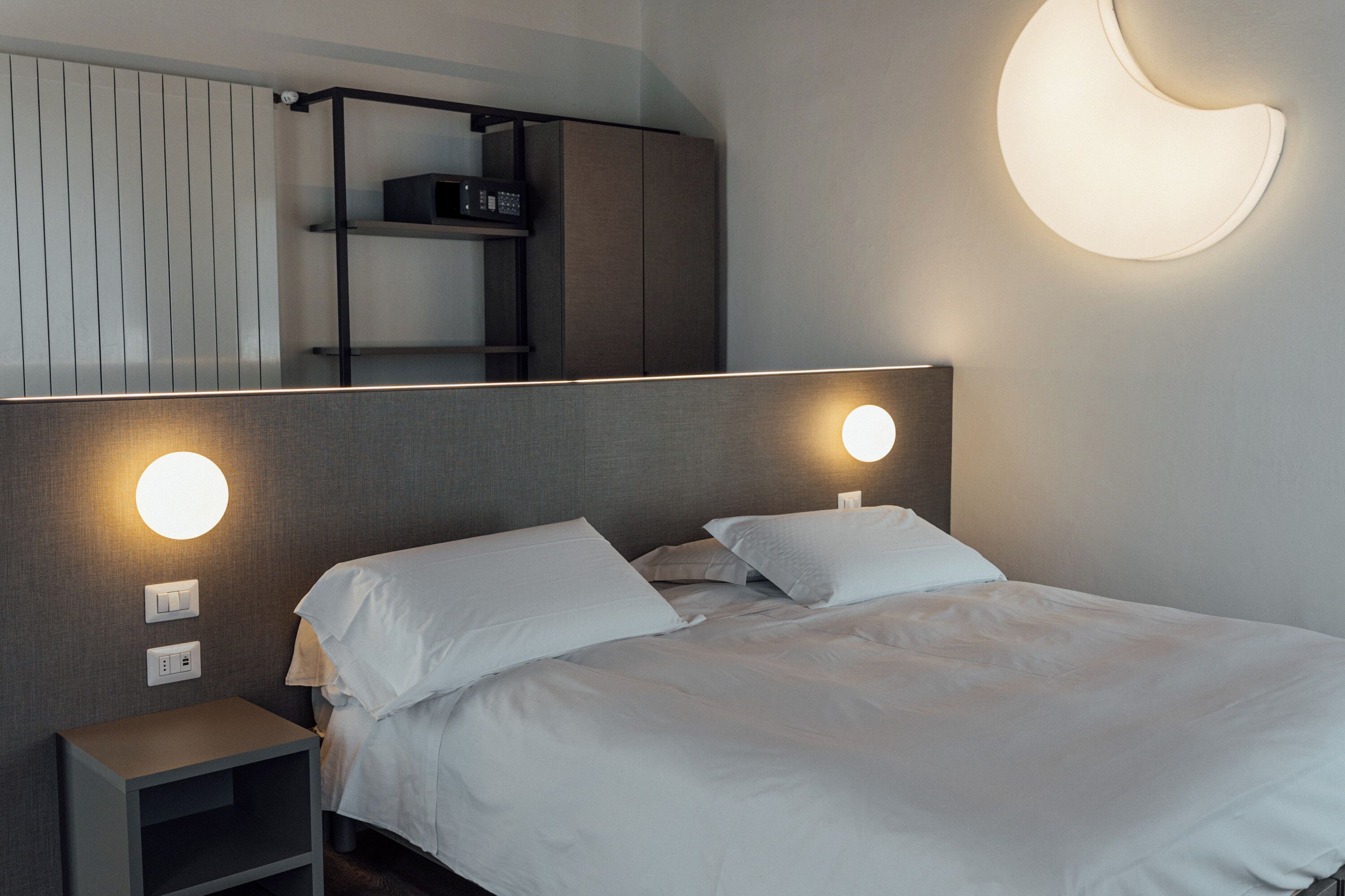 A modern bedroom with a bed, bedside tables, and a wall-mounted light fixture.