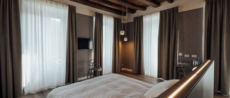 A modern hotel room with a wooden ceiling, a large bed, a desk with a chair, and a TV.