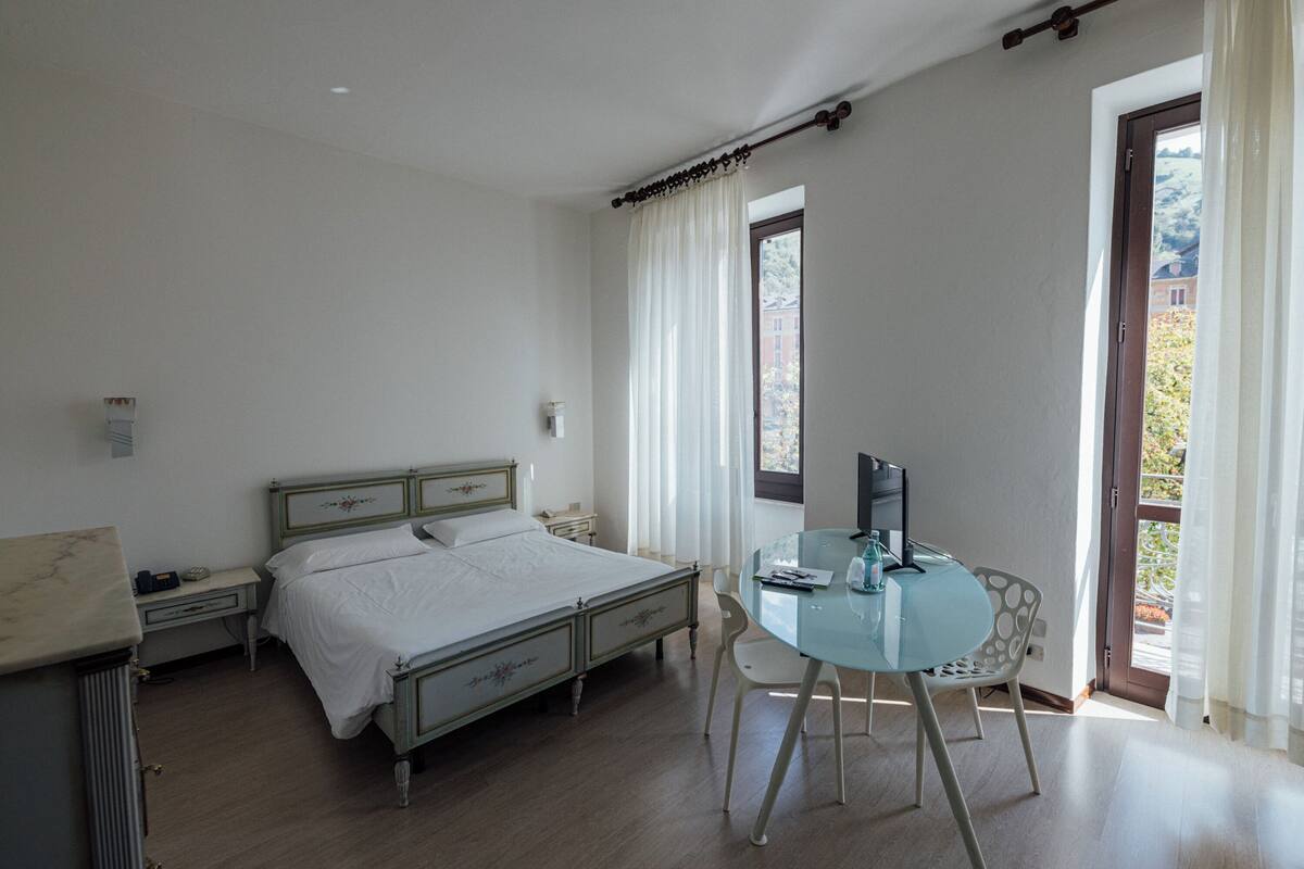 Un dormitorio con cama, mesita de noche, silla y una pequeña mesa con televisor.