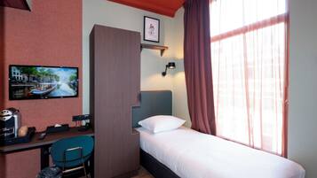 A hotel room with a bed, a desk with a chair, a television, and a window with curtains.