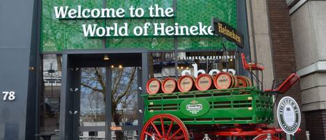 A building entrance with a sign reading "Welcome to the World of Heineken" and a green carriage with barrels.