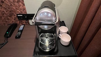 Una cafetera con jarra de vidrio, dos tazas blancas y una bandeja con diferentes cápsulas de café.