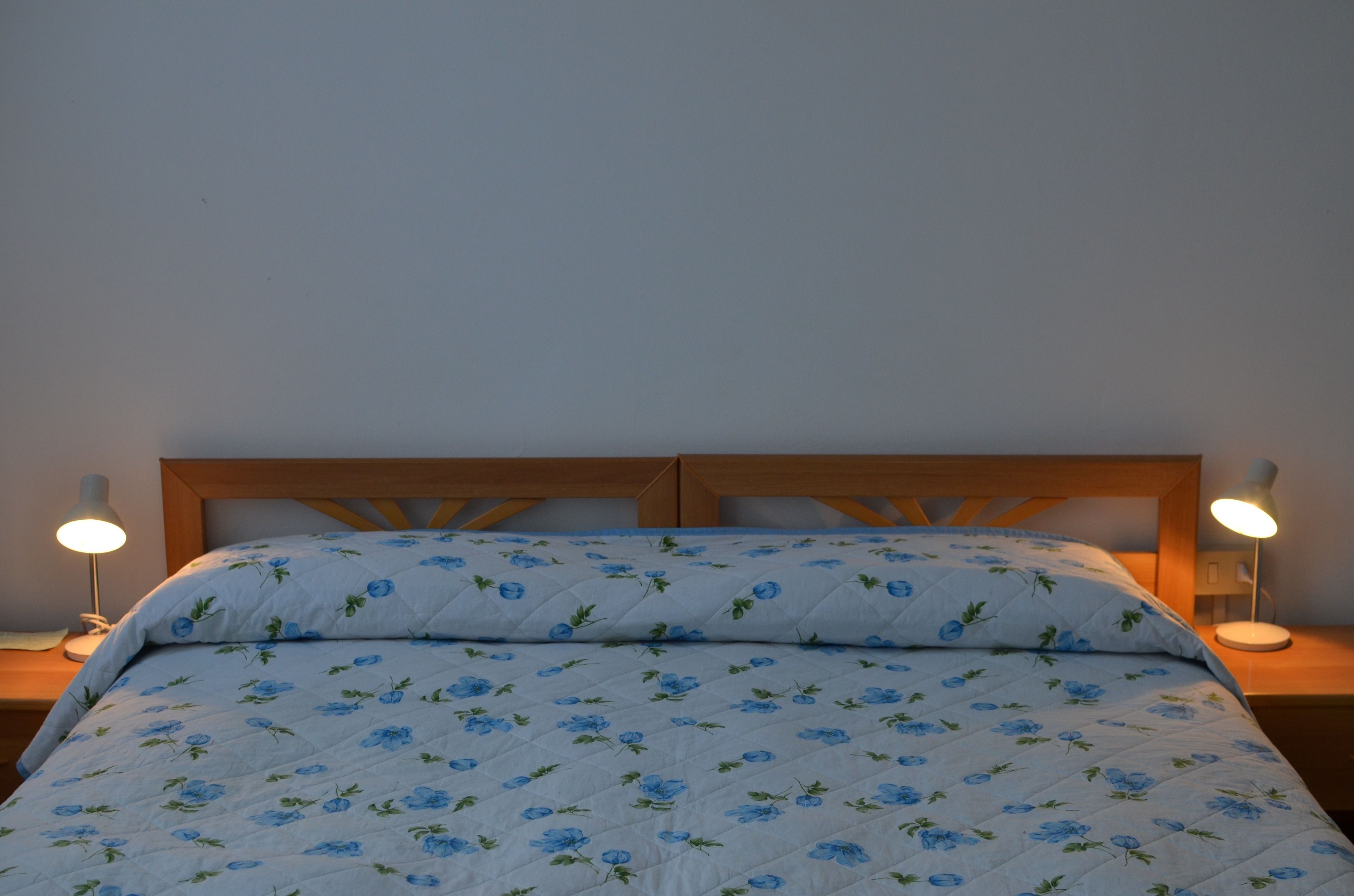Una cama con colcha estampada y dos lámparas de noche.