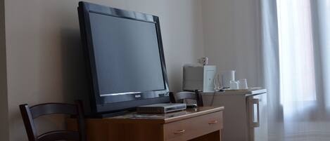 Une pièce comprenant un bureau, une télévision, une chaise, un petit meuble et une fenêtre avec des rideaux.