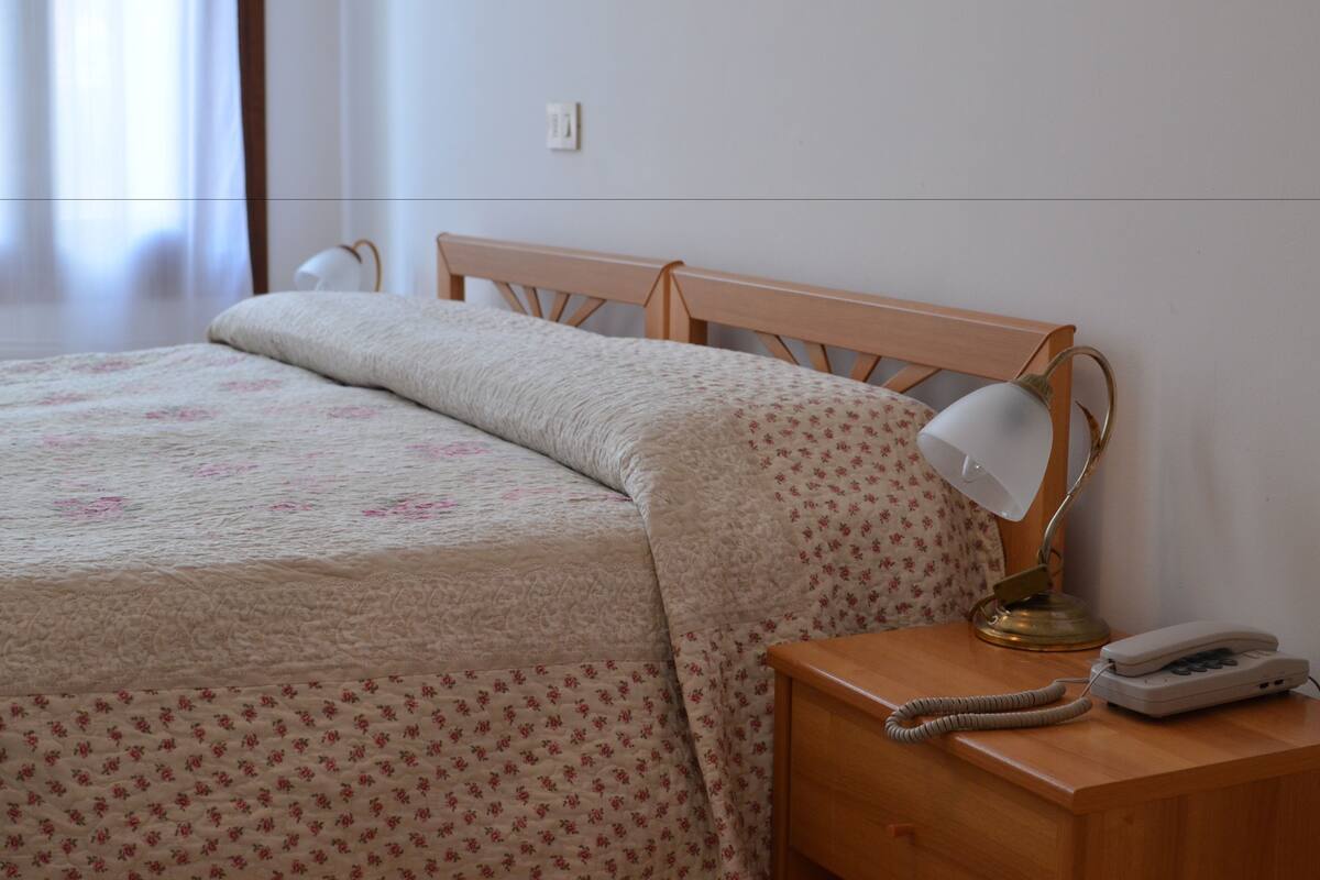 A neatly made bed with a floral-patterned bedspread, a bedside lamp, and a telephone on a wooden nightstand.