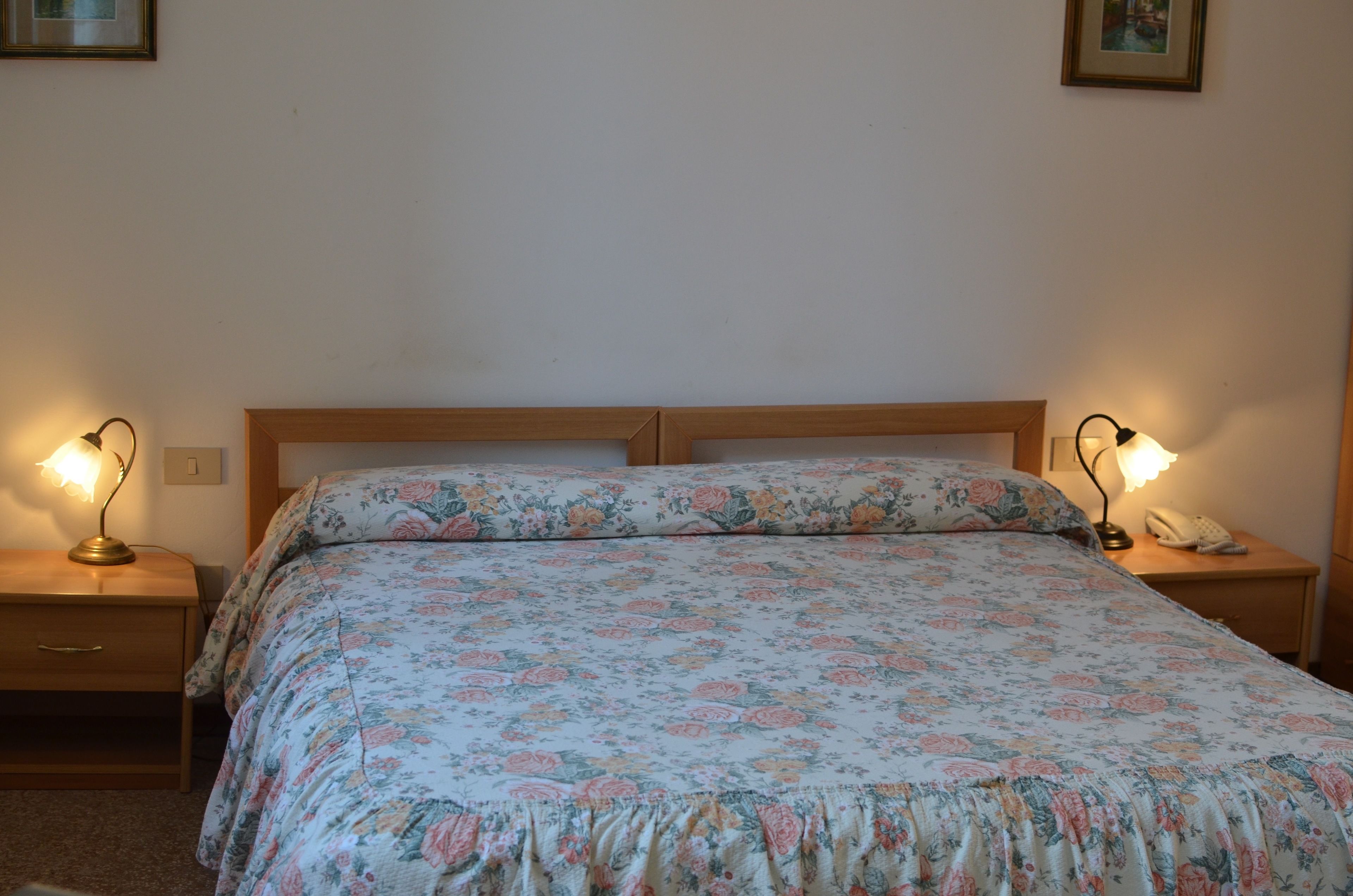 Ein Schlafzimmer mit blumigem Bettbezug, zwei Nachttischlampen, einem Holznachttisch und einem Telefon.