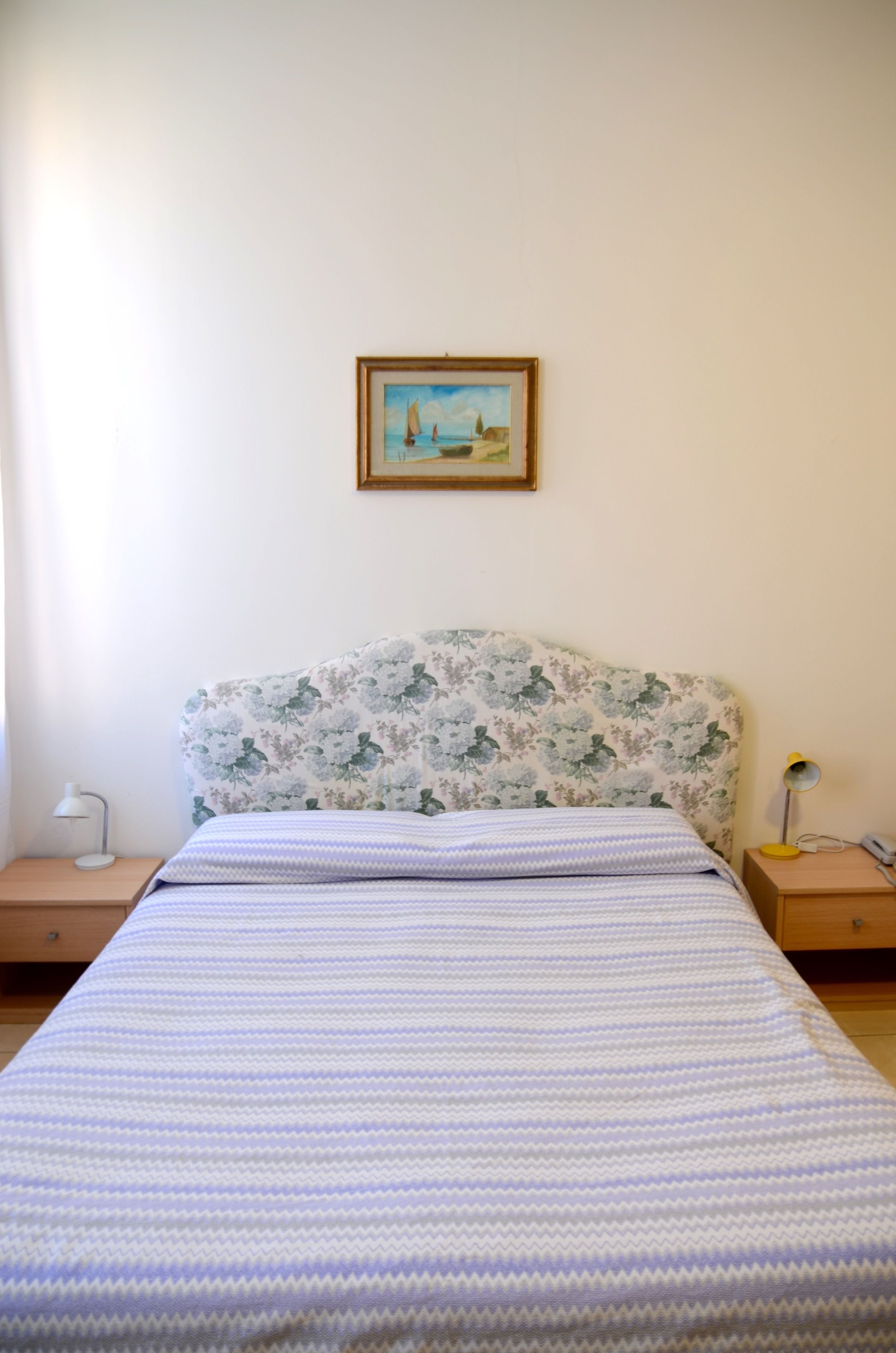 Ein Schlafzimmer mit einem blumigen Kopfteil, einer gestreiften Bettdecke, einem gerahmten Gemälde an der Wand und Nachttischlampen.