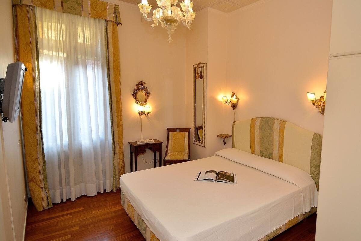 Habitación de hotel con una cama grande, una mesita de noche con lámpara, un espejo y un armario.