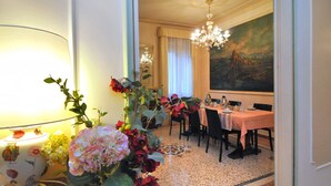 Un comedor con una mesa preparada para cuatro personas, una araña y un cuadro grande en la pared.