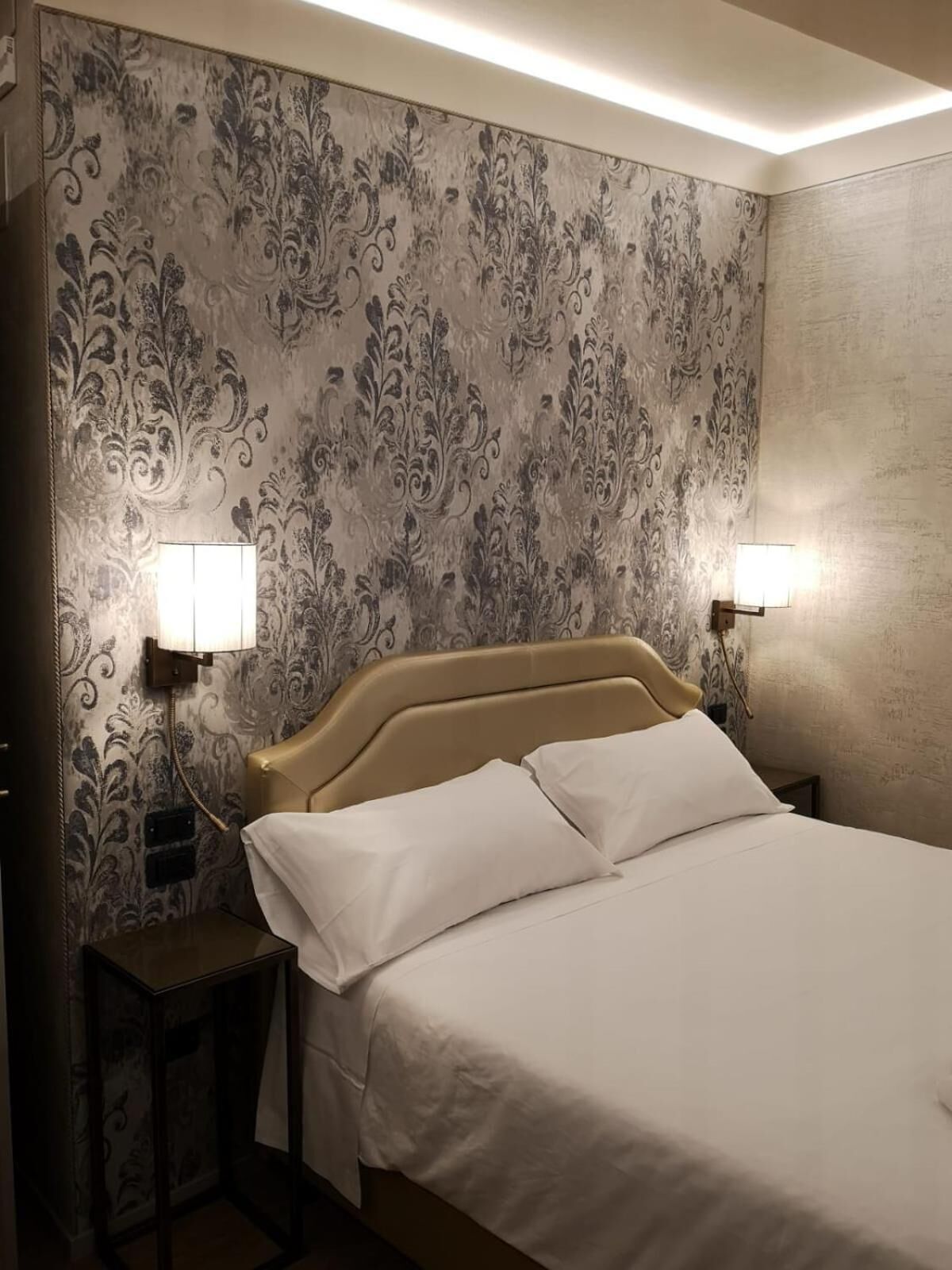 Une chambre d’hôtel avec un lit, deux lampes de chevet et un papier peint à motifs.