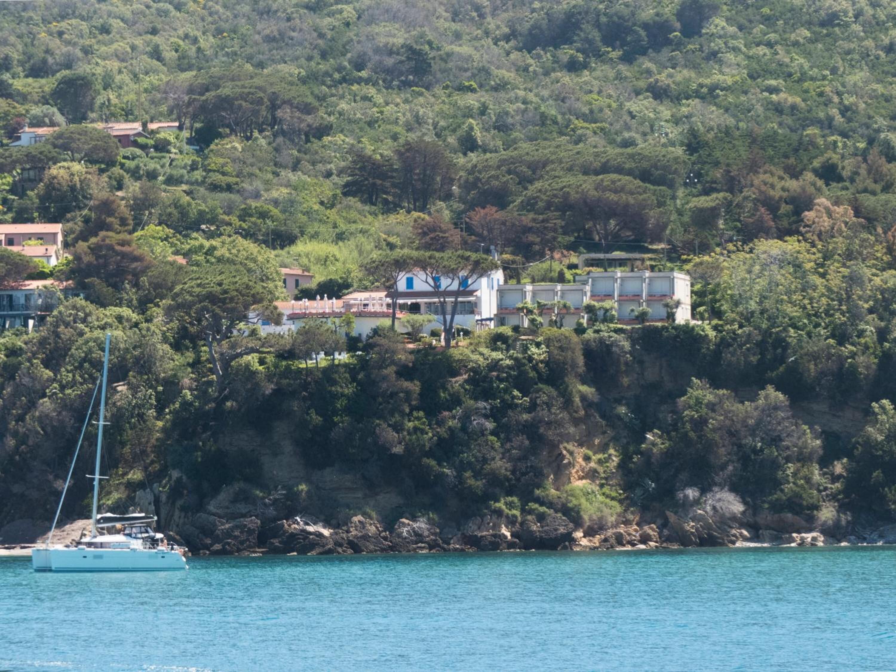 Una propiedad costera con vista al acantilado, un velero en el agua y un edificio con varios balcones que dan al mar.