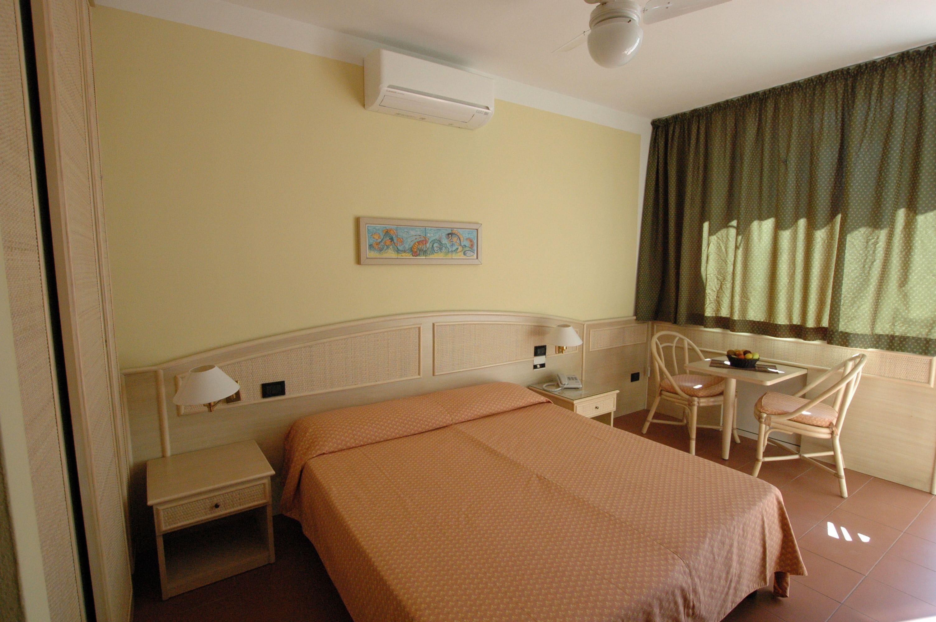 A hotel room with a bed, bedside table, lamp, chair, and a small table with a fruit bowl.
