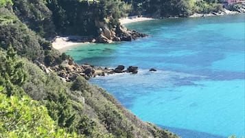 Paesaggio costiero con edifici su una collina, mare cristallino e vegetazione lussureggiante.