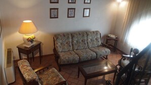 Ein Wohnzimmer mit einer Couch, Sesseln, einem Couchtisch, einer Lampe und gerahmten Bildern an der Wand.