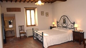 Ein Schlafzimmer mit Bett, Nachttischen, einem Sessel, einem Fenster und einem Spiegel.