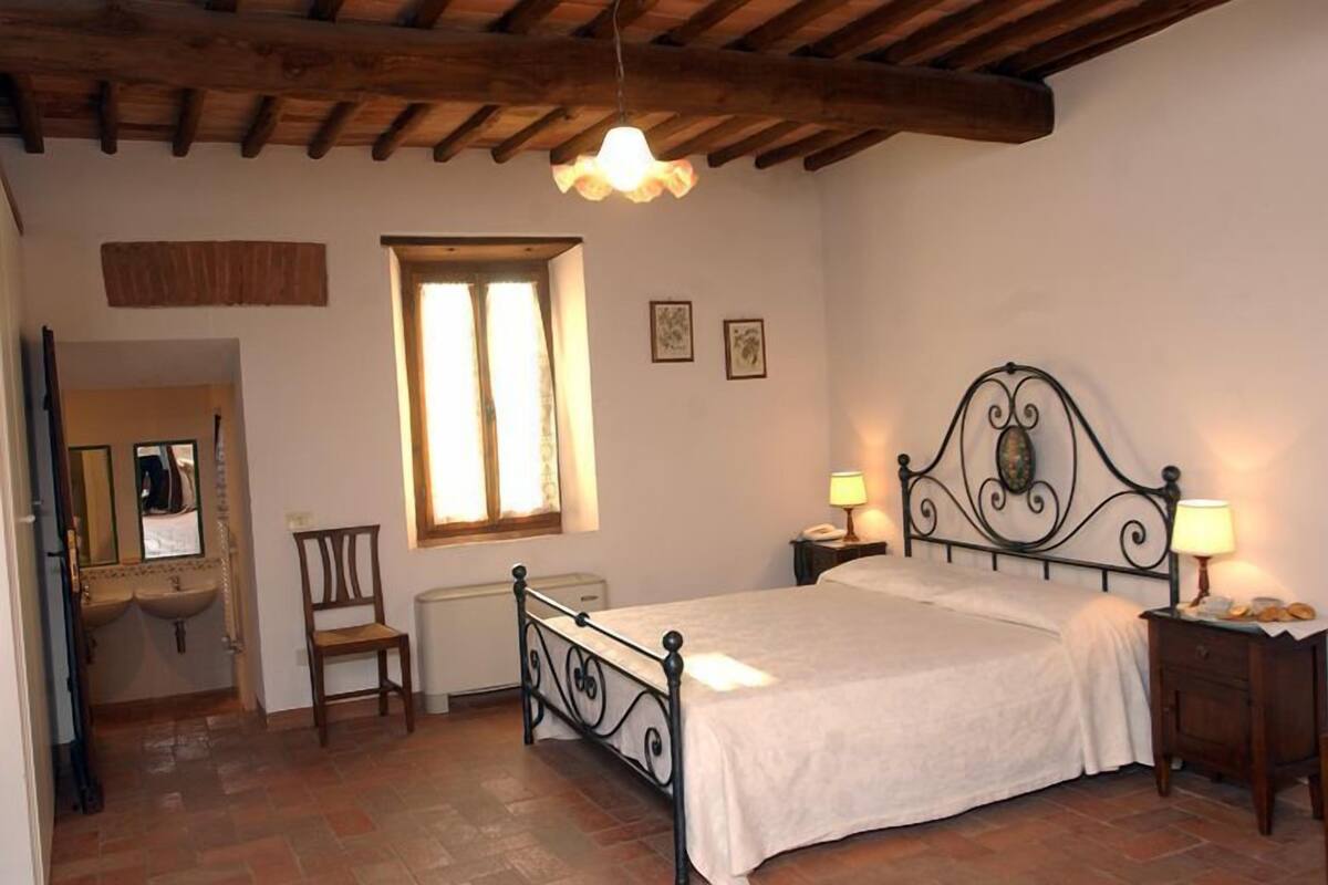 Quarto com cama, mesas de cabeceira, uma cadeira, janela e espelho.