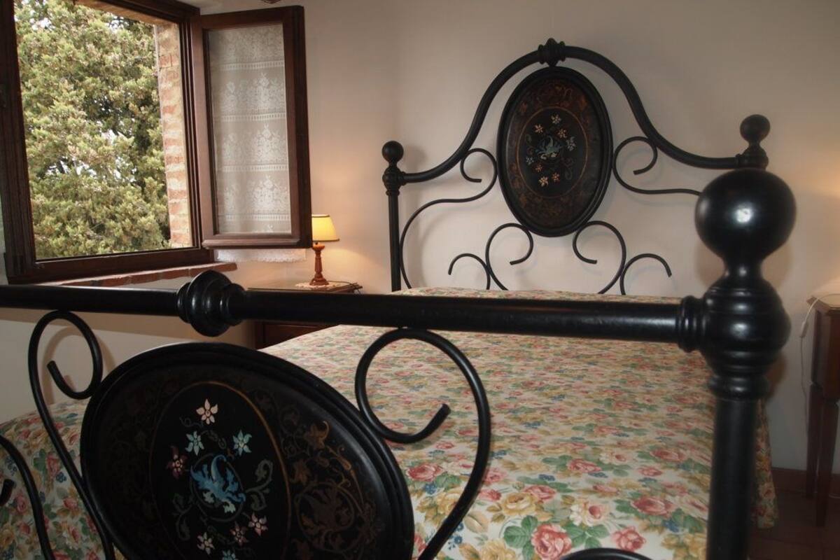 Uma cama com colcha florida, cabeceira com prato decorativo e janela com vista para árvores.