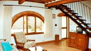 Ein Wohnzimmer mit einer Couch, einem Sessel und einem Couchtisch. Eine Treppe führt in einen anderen Raum.