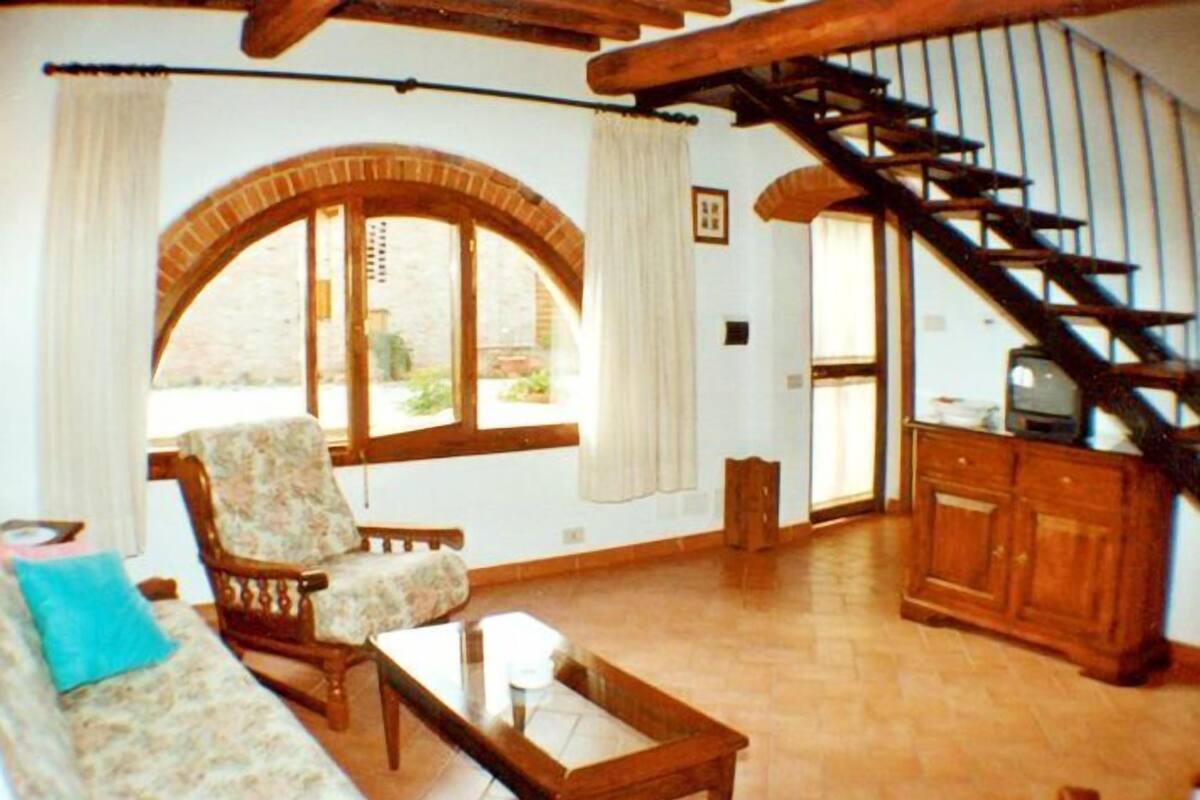 Uma sala de estar com sofá, poltrona e mesa de centro. Escada leva a outro cômodo.