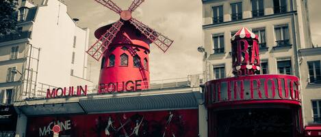 Moulin Rouge-byggnaden med en väderkvarn på taket, stora röda blommor i krukor och en skylt för restaurangen.