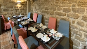 A stone-walled dining area with tables set for a meal, featuring blue and pink upholstered chairs.