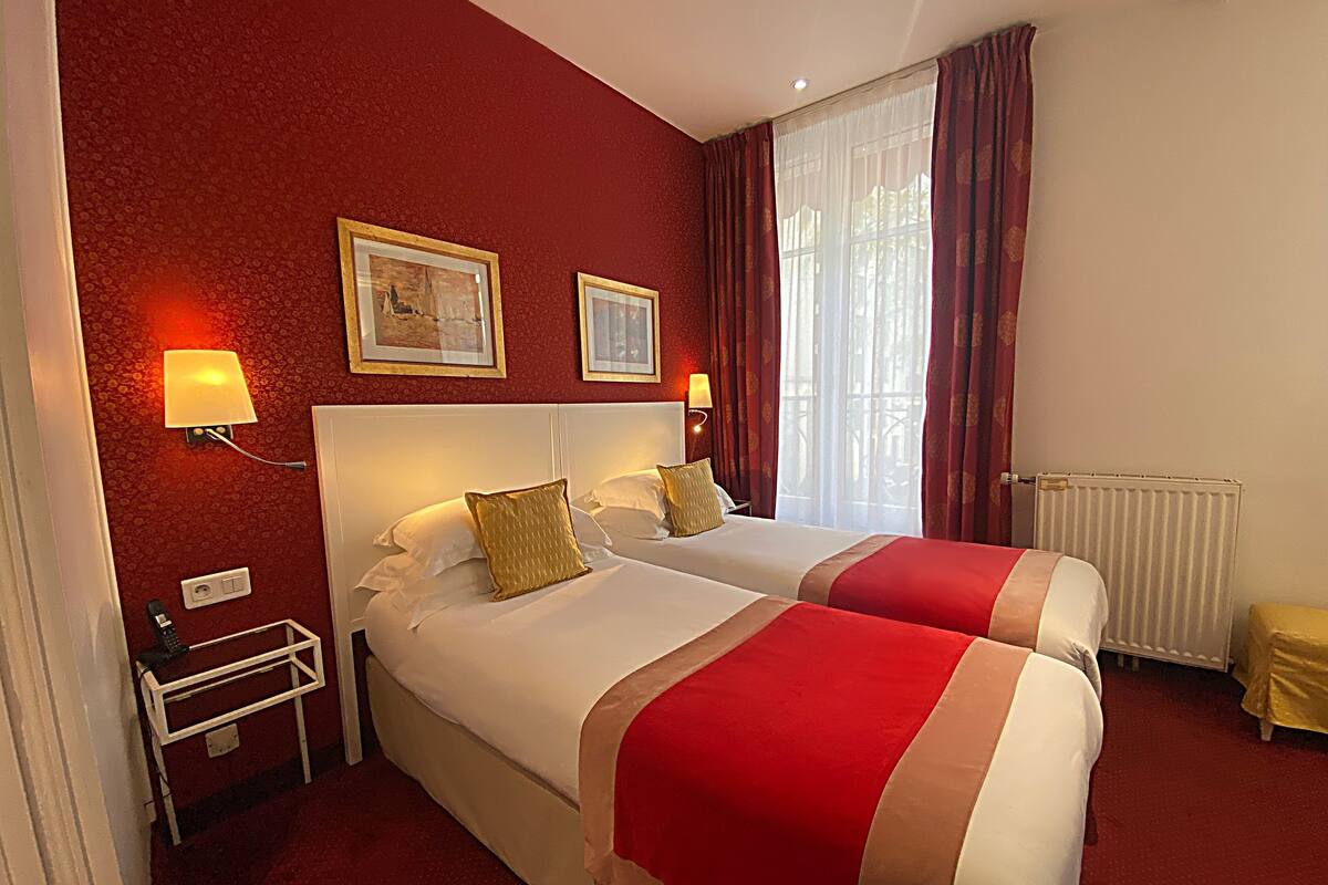Habitación de hotel con dos camas, paredes rojas y una ventana con cortinas.