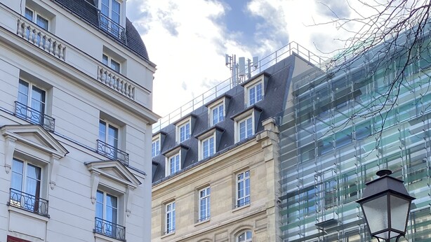 A multi-story building with a classical facade, including ornate balconies and a modern glass structure on the right.