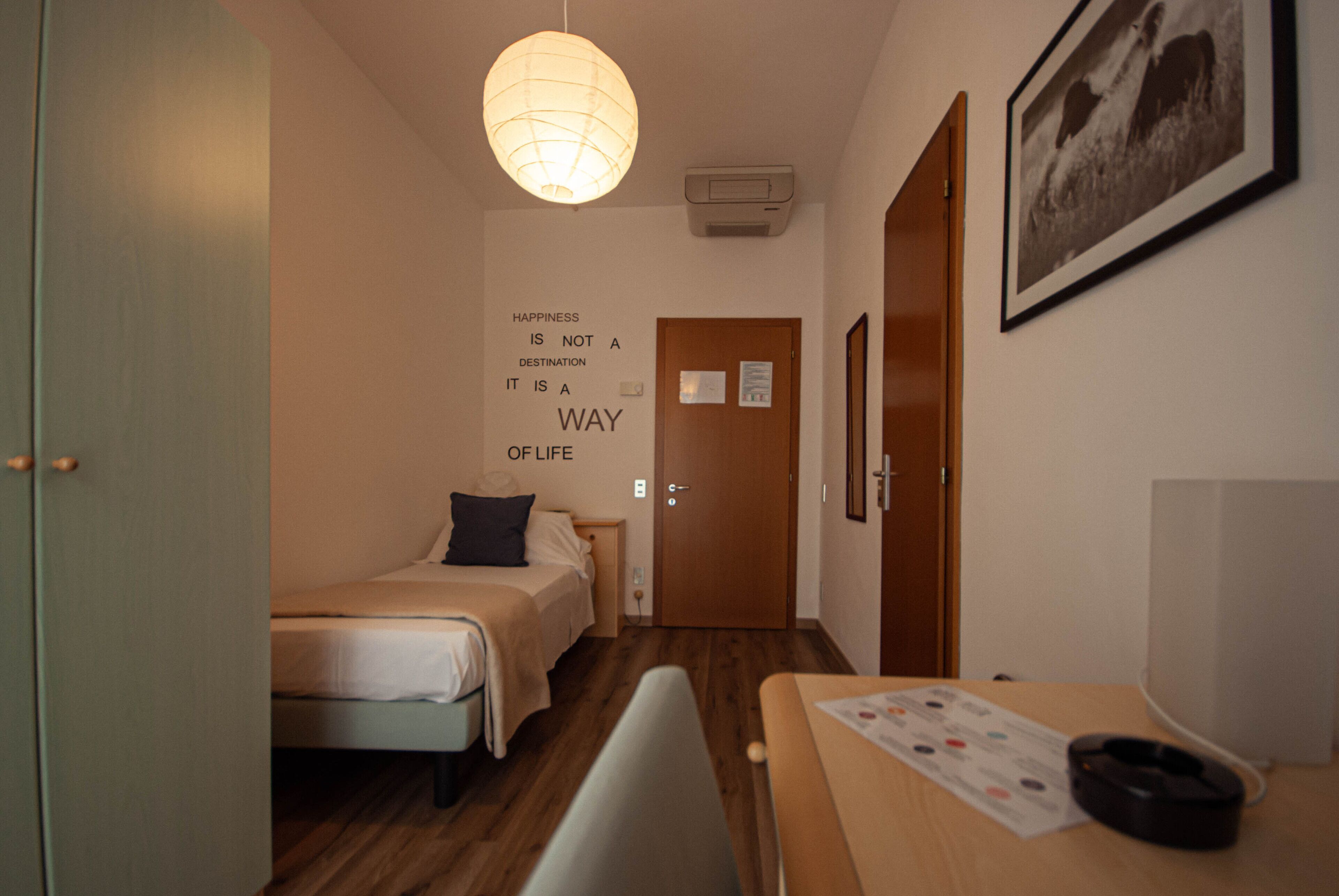 Una habitación de hotel con cama, escritorio, silla, lámpara de pared, un cuadro enmarcado y una cita motivacional en la pared.