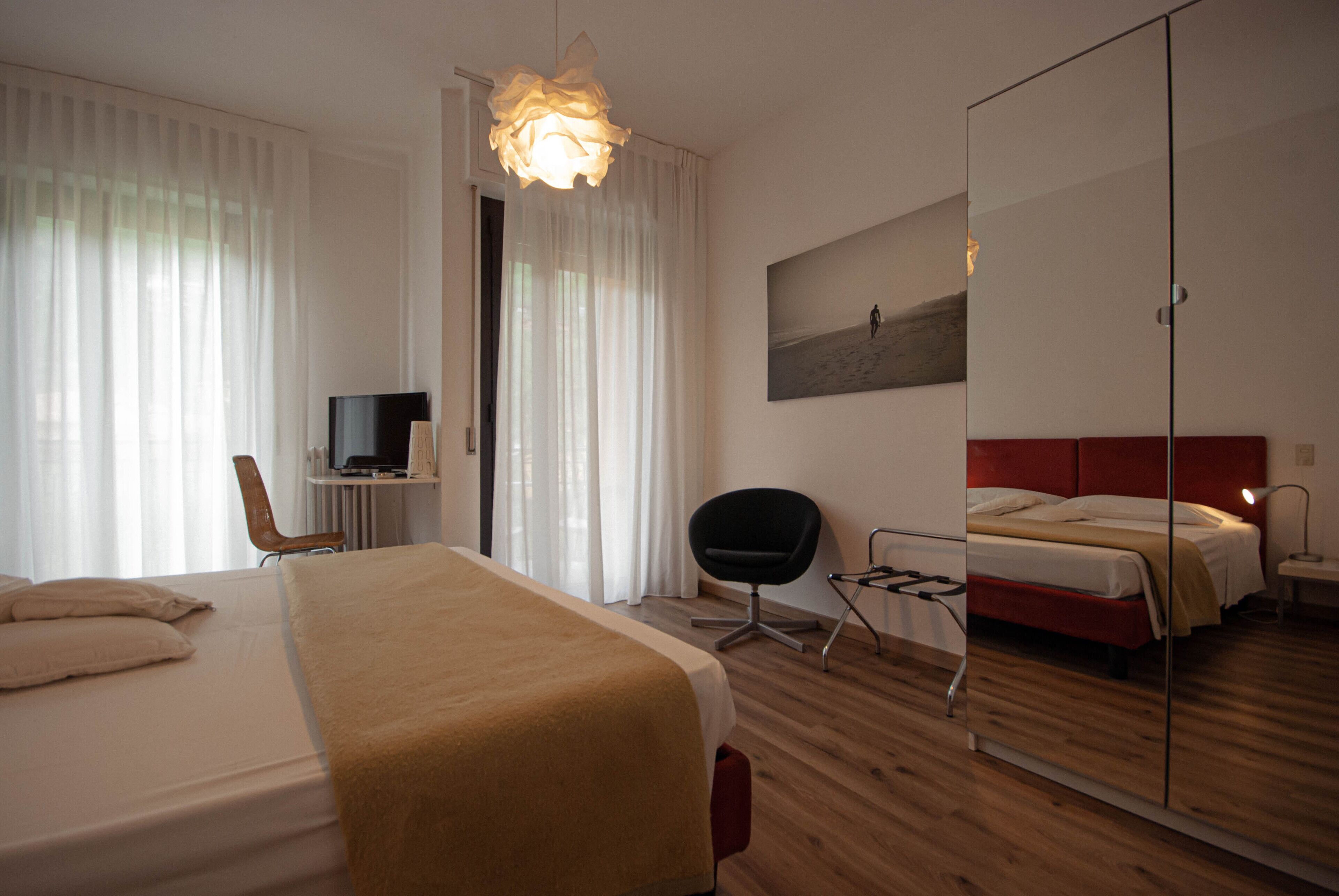 Ett hotellrum med en stor säng, ett skrivbord med en stol, en tv och en spegel.
