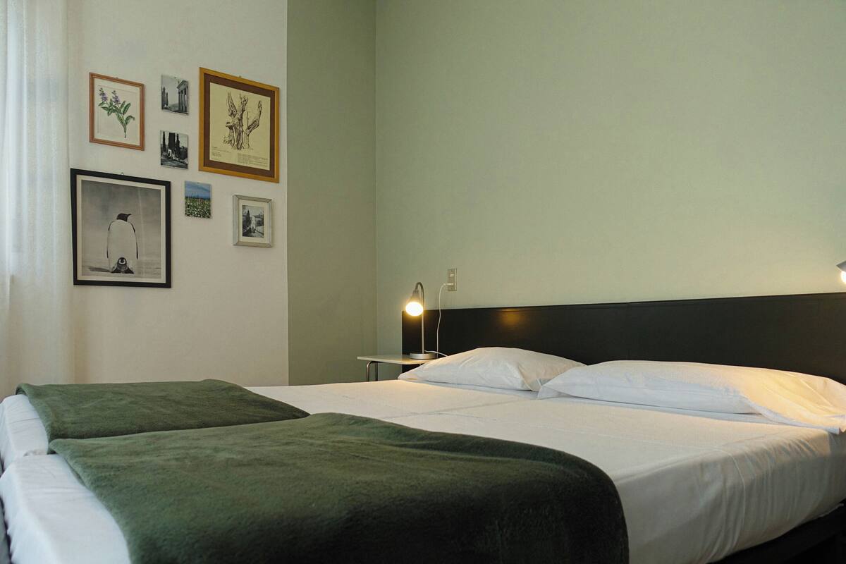 A hotel room with two beds, a nightstand, and a wall adorned with framed pictures.