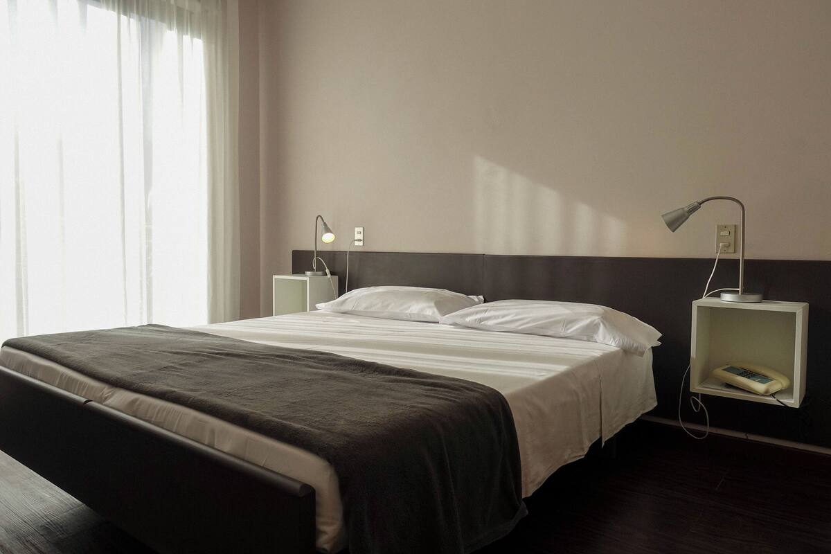 A neatly made bed with a dark headboard, white bedding, and two bedside tables with lamps and a phone.