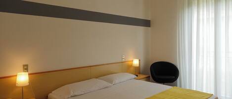 A hotel room with a bed, bedside lamps, a chair, and a window with curtains.