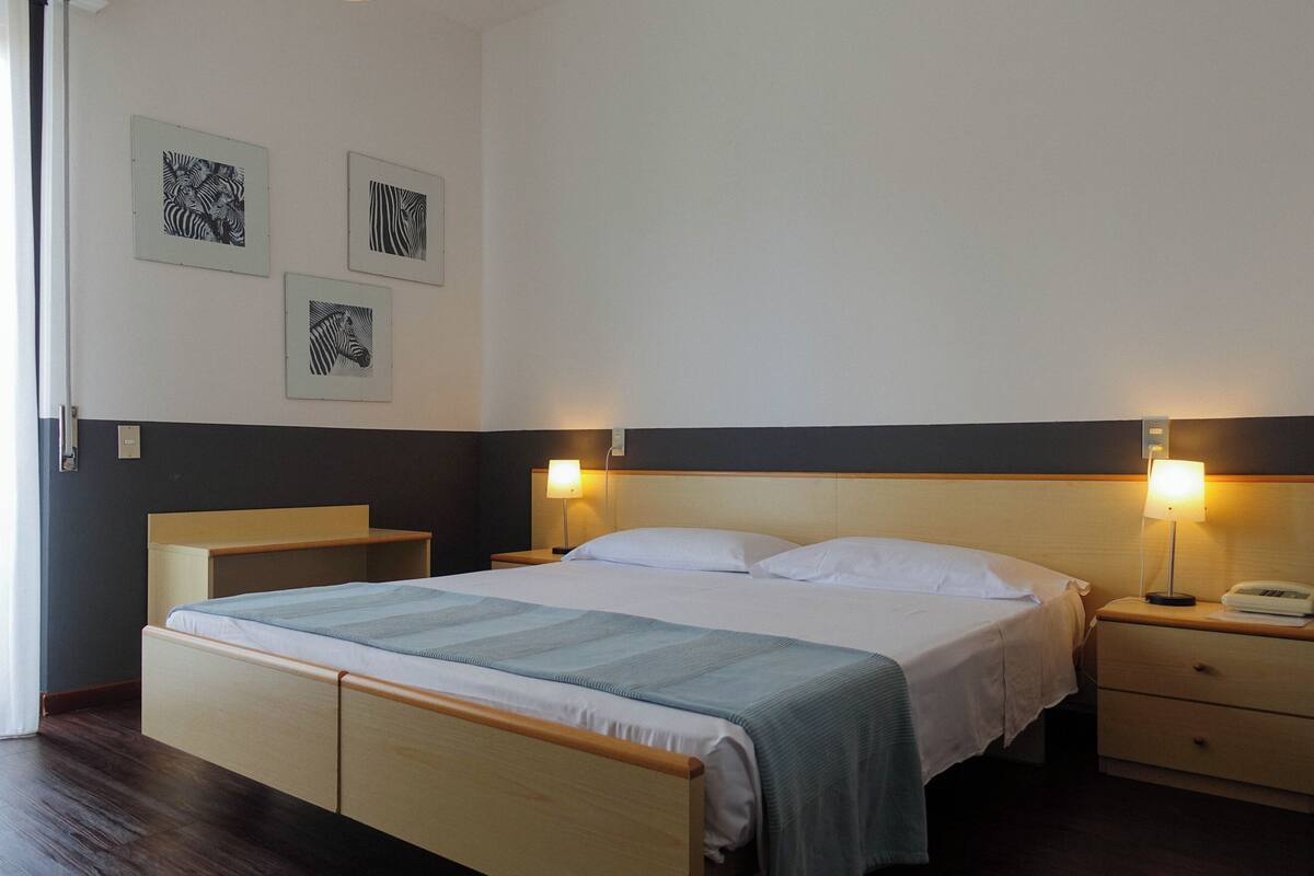 A hotel room with a bed, bedside tables, and wall-mounted artwork.