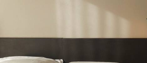 Un lit avec du linge de lit blanc et une tête de lit sombre, dans une pièce dont le mur est d’une couleur neutre.