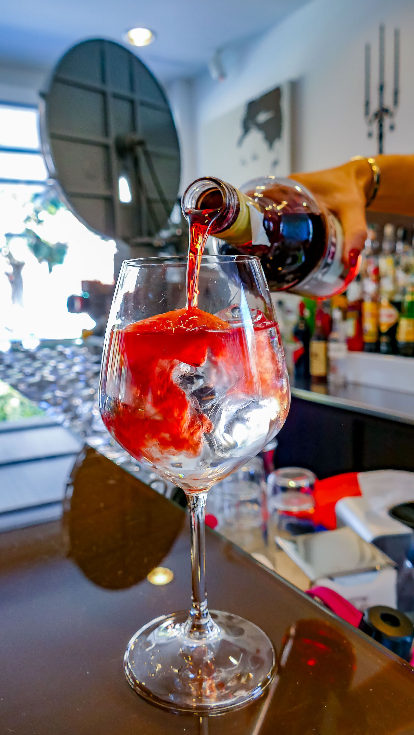 A hand pouring a red liquid into a clear glass.