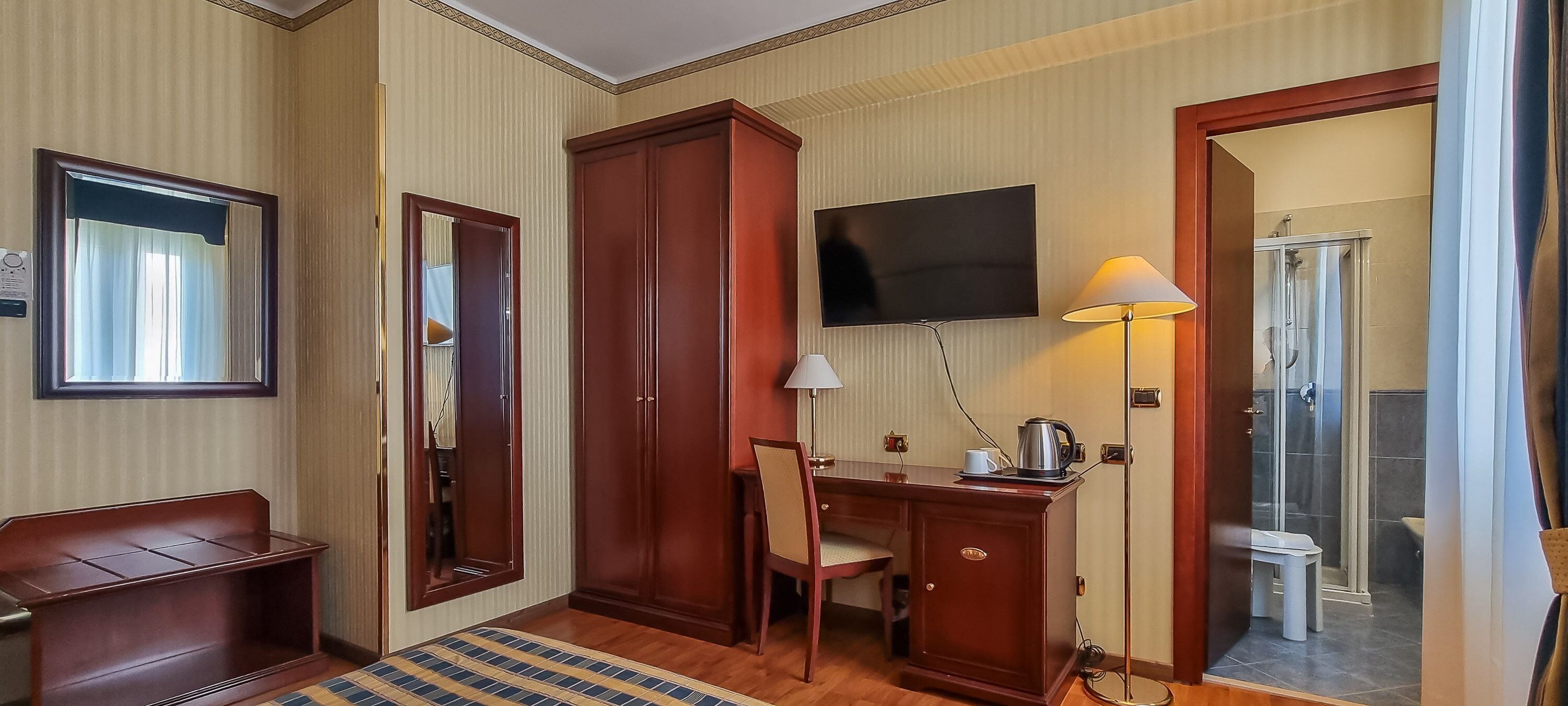 A hotel room with a wooden desk, a chair, a television, a lamp, and a shower area.